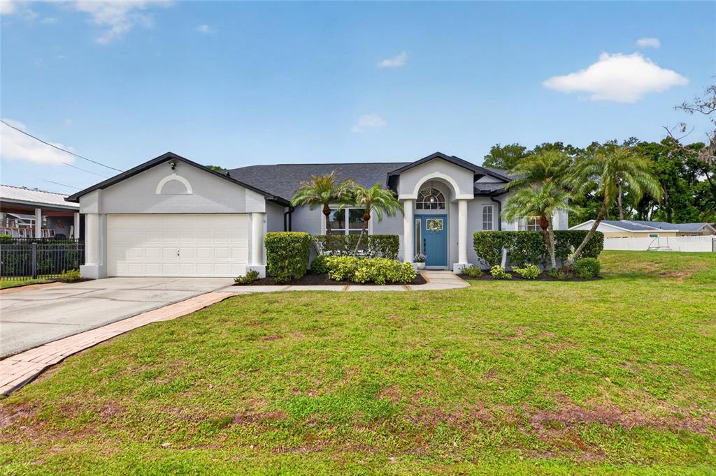 A single-story house with a two-car garage, blue front door, and palm trees — 21865 OCEAN PINES DRIVE, LAND O LAKES, FL