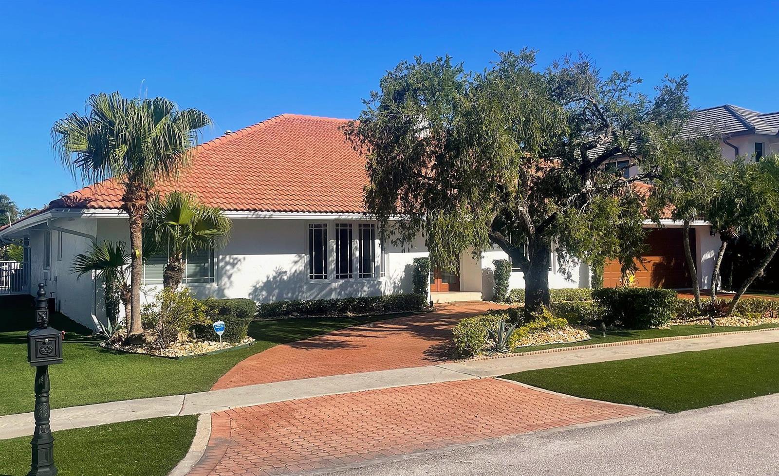 A single-story house with a terracotta tile roof, white stucco walls, and a brick driveway — 885 NE Mulberry Drive, Boca Raton FL 33487, BOCA RATON, FL