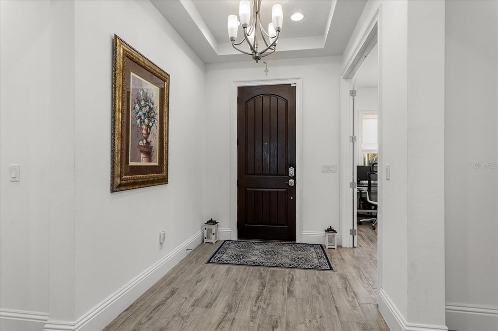 An entryway features a dark wood front door, light wood-look flooring, and a chandelier — 13283 ALDERLEY DRIVE, ORLANDO, FL