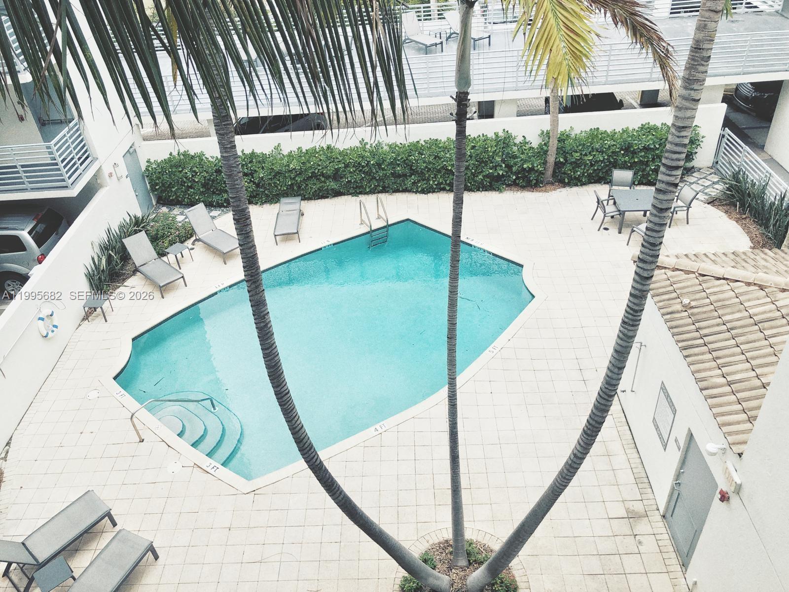 An aerial view shows a swimming pool surrounded by a patio, lounge chairs, and palm trees — 1401 Bay Rd # 412, Miami Beach FL 33139, MIAMI BEACH, FL