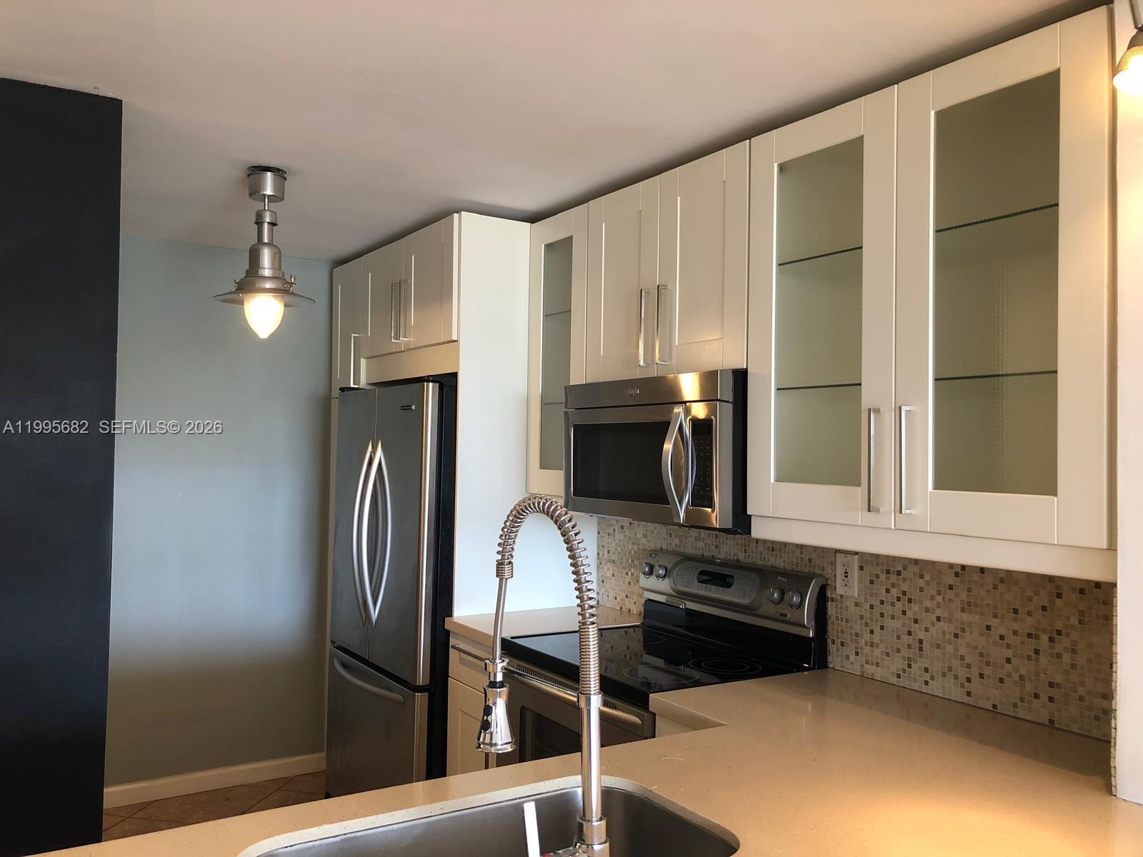 A kitchen features white cabinets, stainless steel appliances, a mosaic backsplash, and quartz countertops — 1401 Bay Rd # 412, Miami Beach FL 33139, MIAMI BEACH, FL