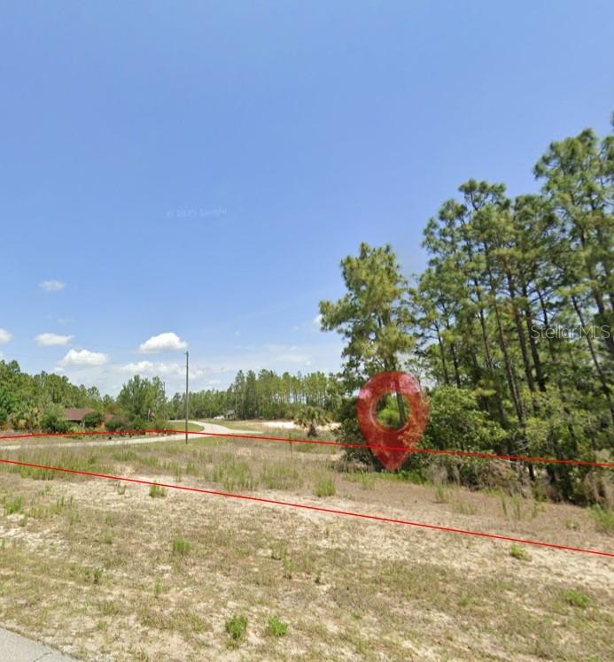 A vacant, grassy lot with scattered trees is outlined by red lines under a blue sky — SW 131ST PLACE, OCALA, FL