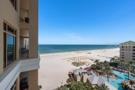An elevated view from a balcony overlooking a sandy beach, ocean, and resort pool area — 11 BAYMONT STREET UNIT 1006, CLEARWATER BEACH, FL