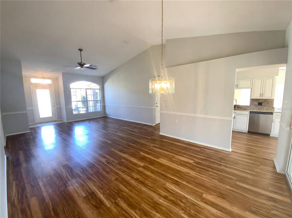 An open-concept living and dining area features vaulted ceilings, wood-look flooring, and a kitchen view — 7410 WILLOW BROOK DRIVE, SPRING HILL, FL