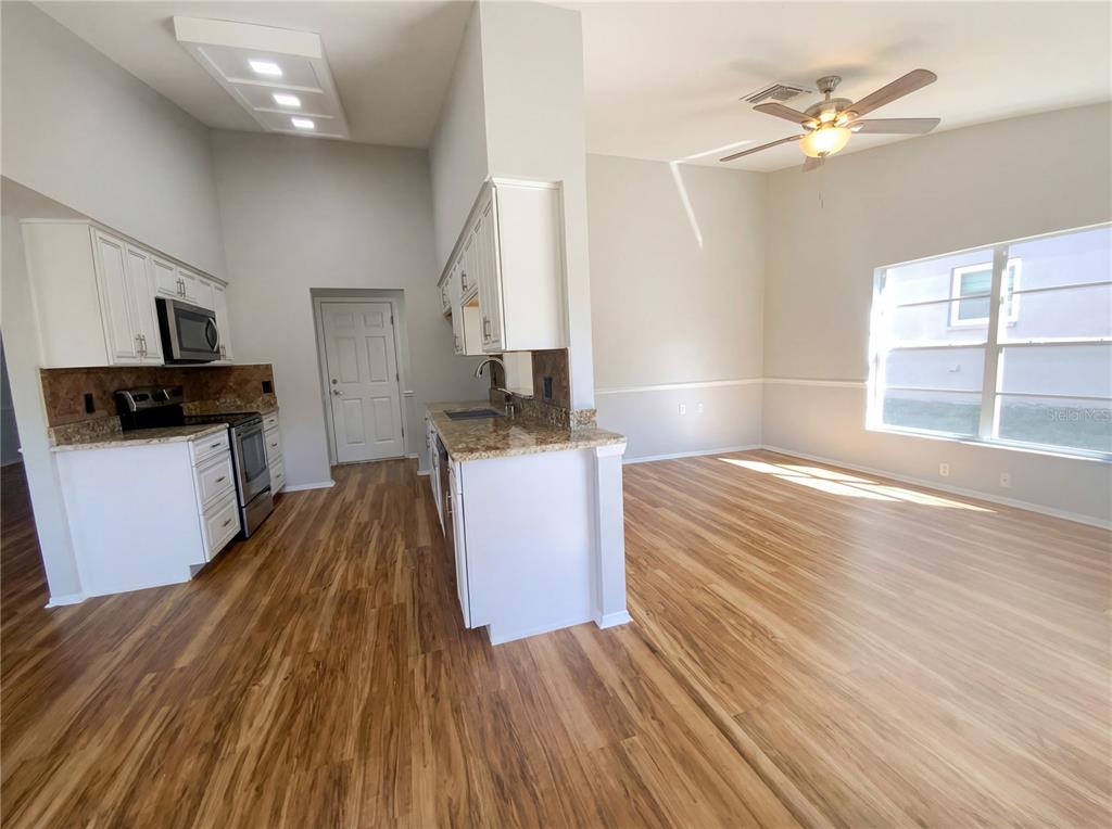 A kitchen with white cabinets and granite countertops opens into a living area with wood flooring — 7410 WILLOW BROOK DRIVE, SPRING HILL, FL