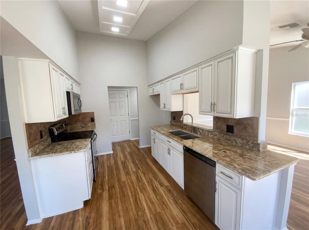 A kitchen with white cabinets, granite countertops, stainless steel appliances, and wood-look flooring — 7410 WILLOW BROOK DRIVE, SPRING HILL, FL