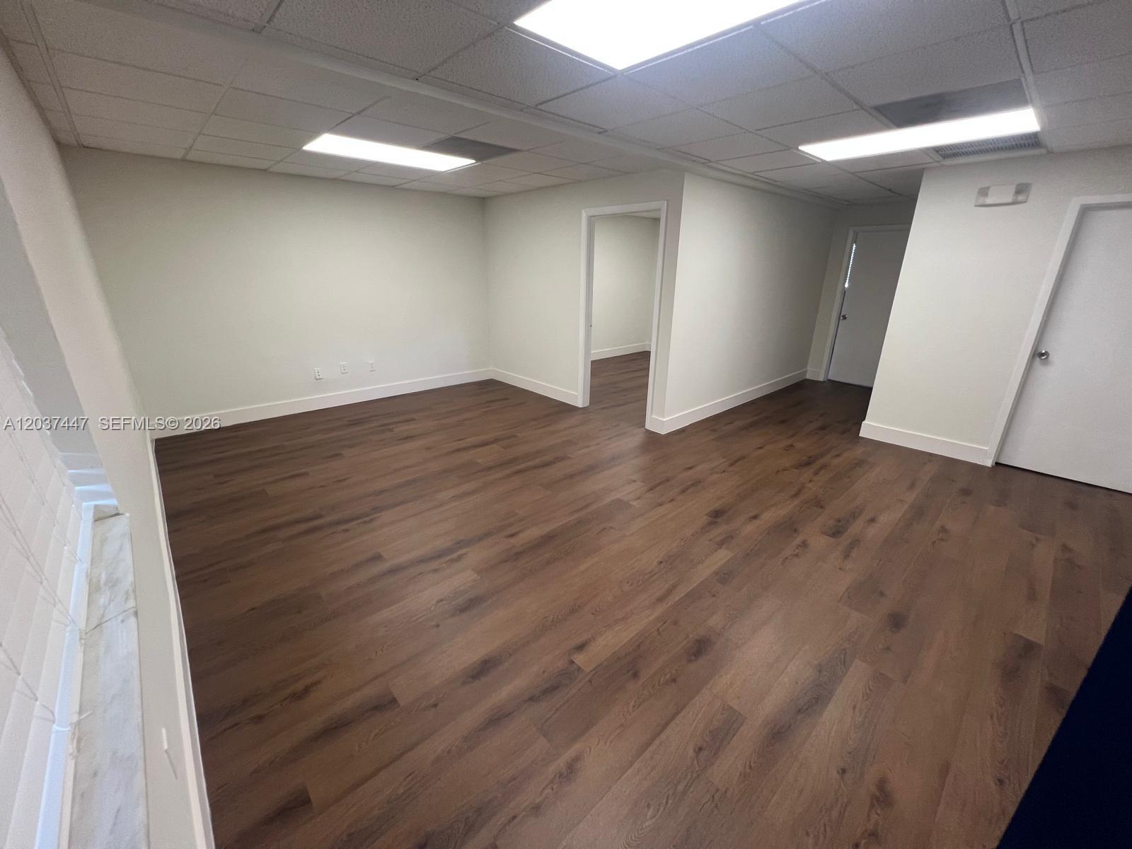 An empty office room features wood-look flooring, white walls, and a drop ceiling with lights — 145 Madeira Ave # 202, Coral Gables FL 33134, CORAL GABLES, FL