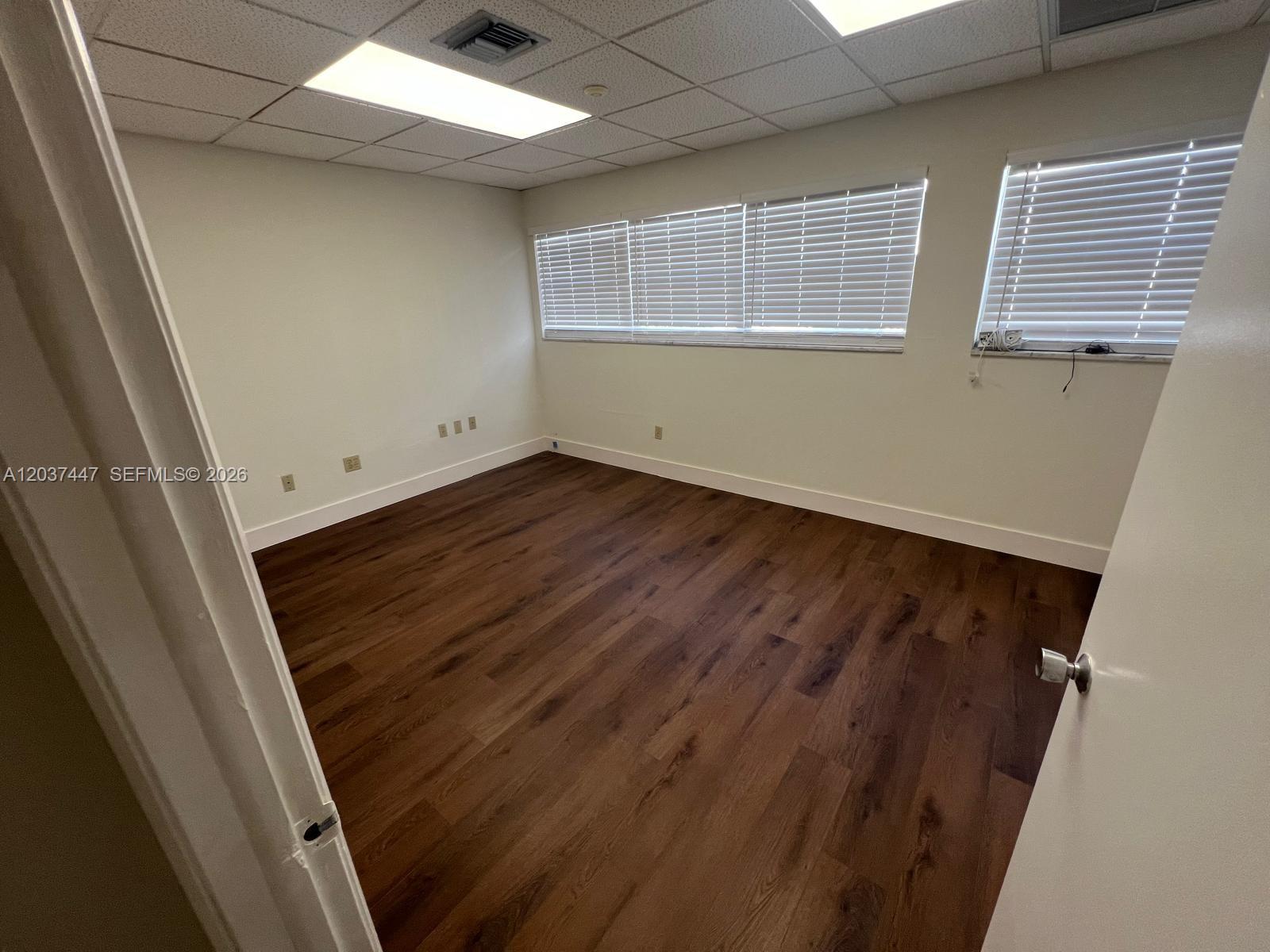 An empty office features dark wood-look flooring, white walls, and a drop ceiling — 145 Madeira Ave # 202, Coral Gables FL 33134, CORAL GABLES, FL