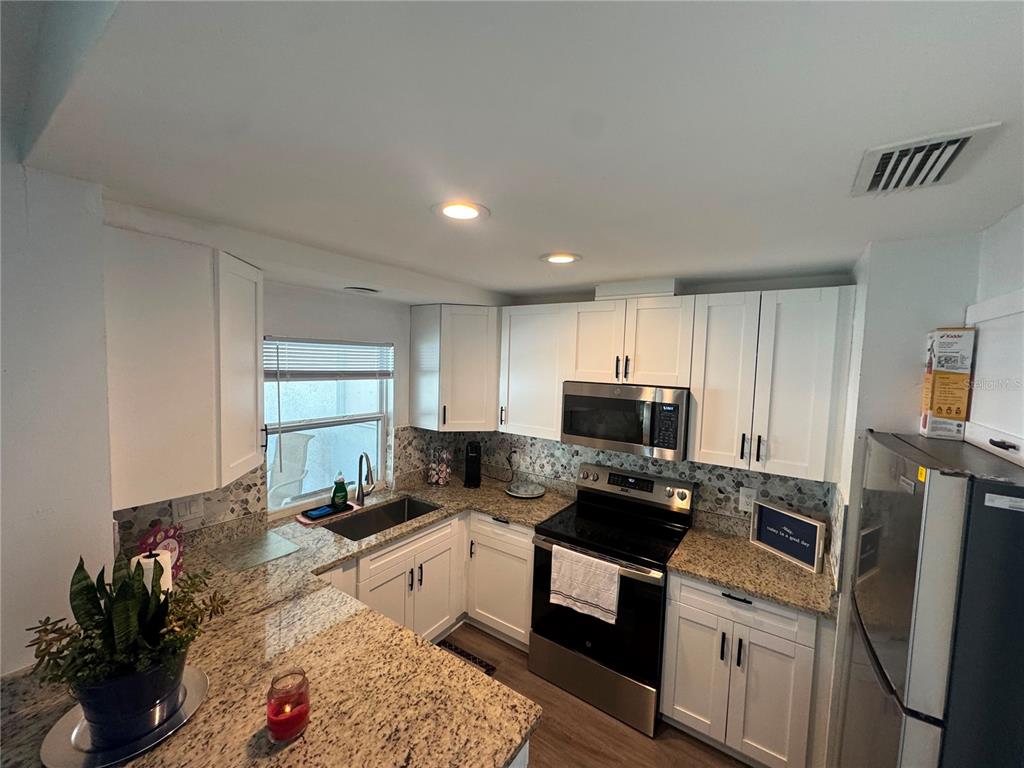 A kitchen features white cabinets, granite countertops, stainless steel appliances, and a window above the sink — 12609 130TH STREET, LARGO, FL