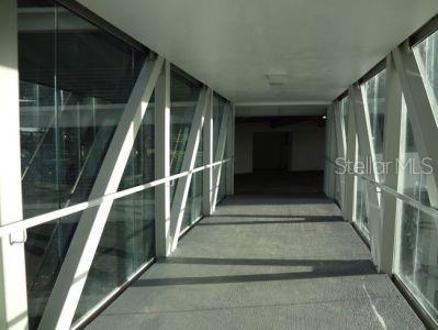 A modern, enclosed pedestrian walkway features glass walls, white structural beams, and gray carpeted flooring — 1500 F.D. ROOSEVELT AVE., GUAYNABO, PR