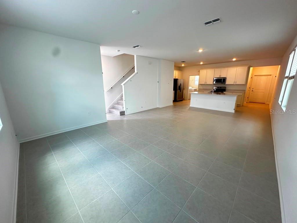 An open-concept living area features light gray tile flooring, a staircase, and a white kitchen — 6099 WELLBEING WAY, CLERMONT, FL
