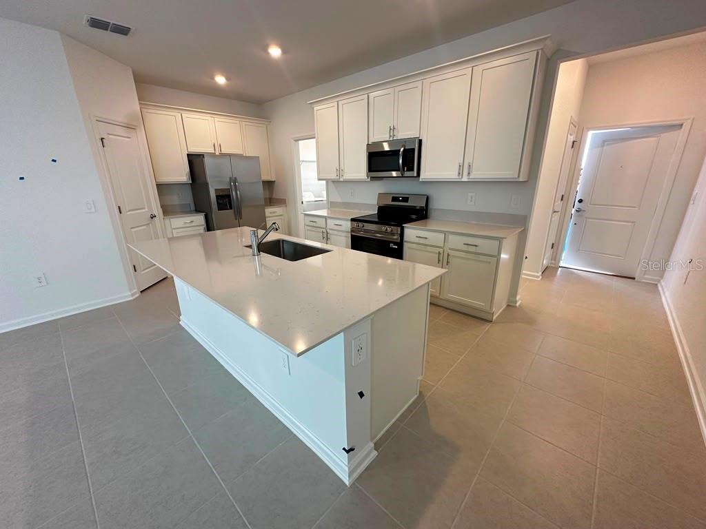 A modern kitchen features white cabinets, stainless steel appliances, and a large central island — 6099 WELLBEING WAY, CLERMONT, FL
