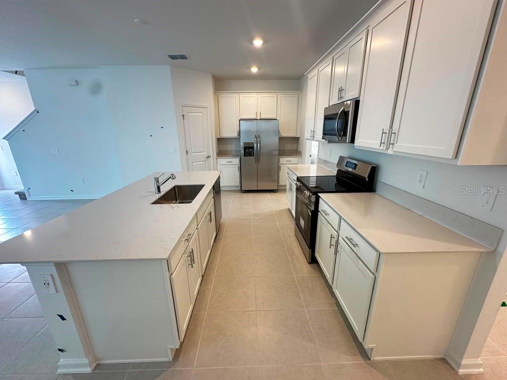 A kitchen with white cabinets, a large island, stainless steel appliances, and light-colored countertops — 6099 WELLBEING WAY, CLERMONT, FL