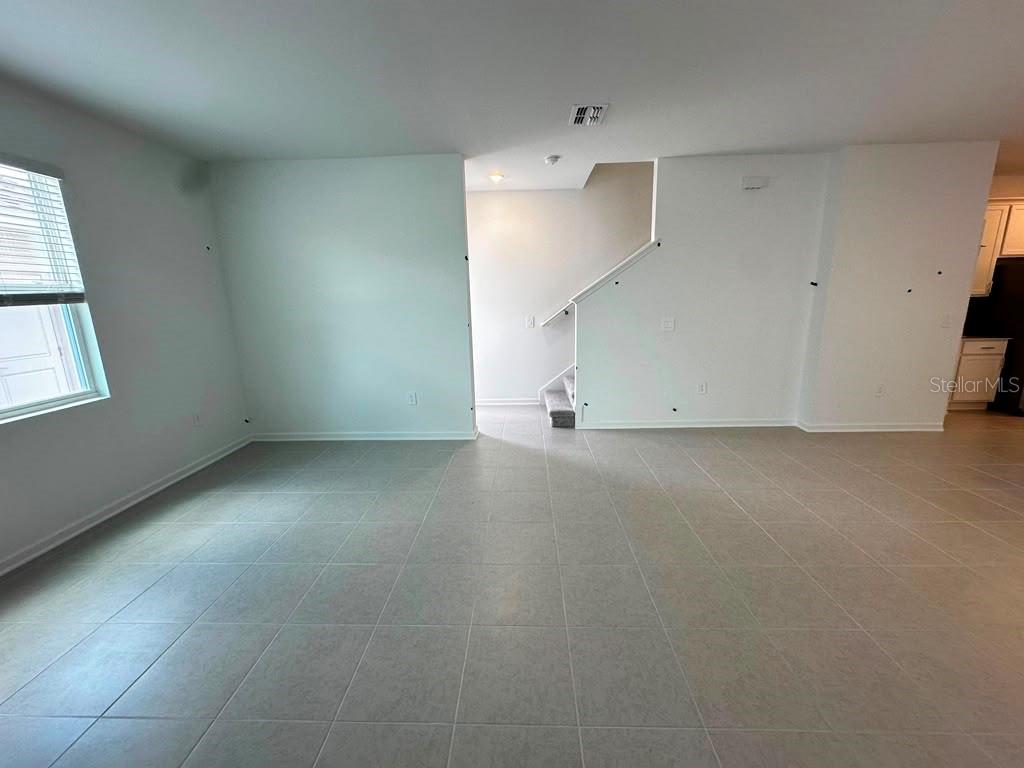 An open living area features light-colored tile flooring, white walls, and a staircase — 6099 WELLBEING WAY, CLERMONT, FL