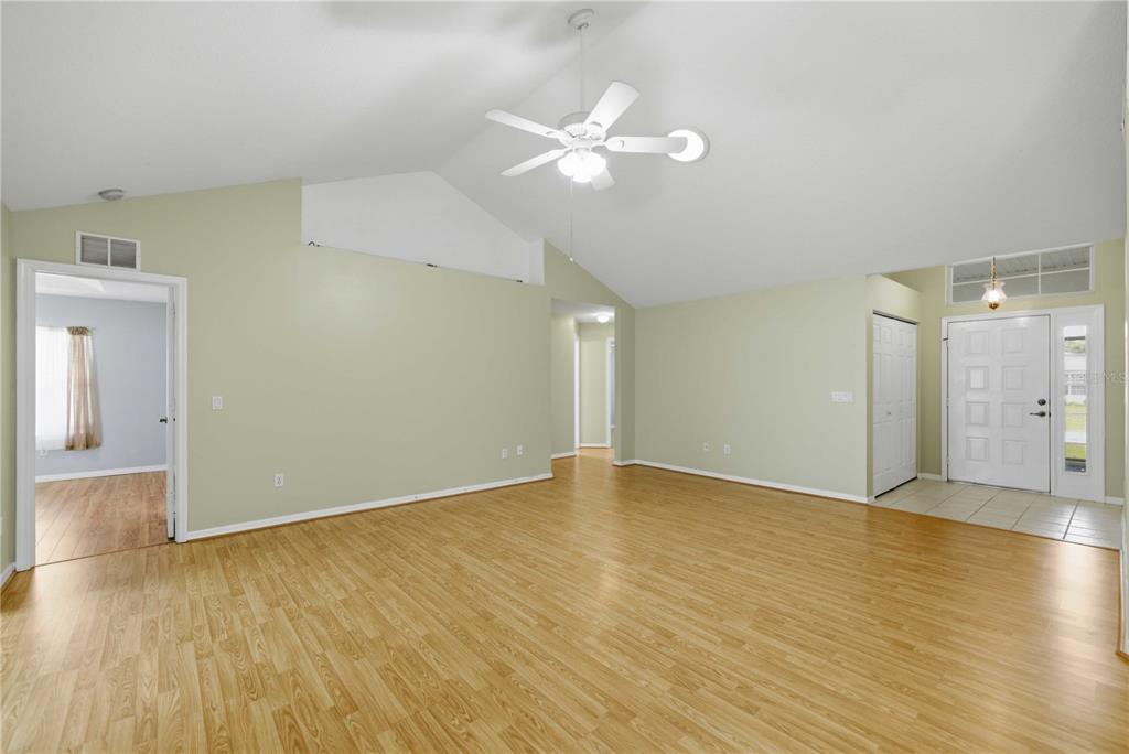 An empty living room features light green walls, vaulted ceilings, and light wood-look flooring — 6181 SW 84TH PLACE, OCALA, FL