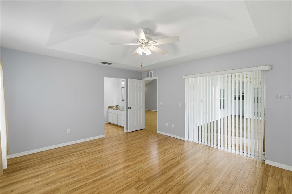A bedroom with light gray walls, wood-look flooring, a tray ceiling, and sliding glass doors — 6181 SW 84TH PLACE, OCALA, FL