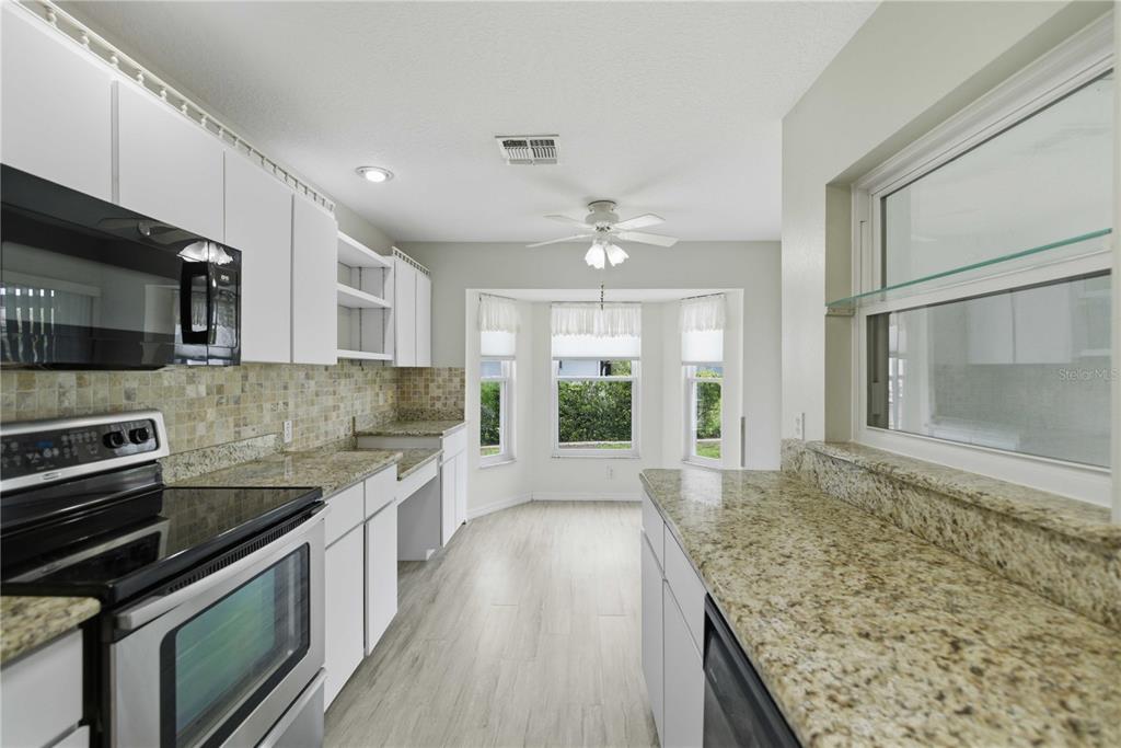A kitchen features white cabinets, granite countertops, a tile backsplash, and a breakfast nook area — 6181 SW 84TH PLACE, OCALA, FL