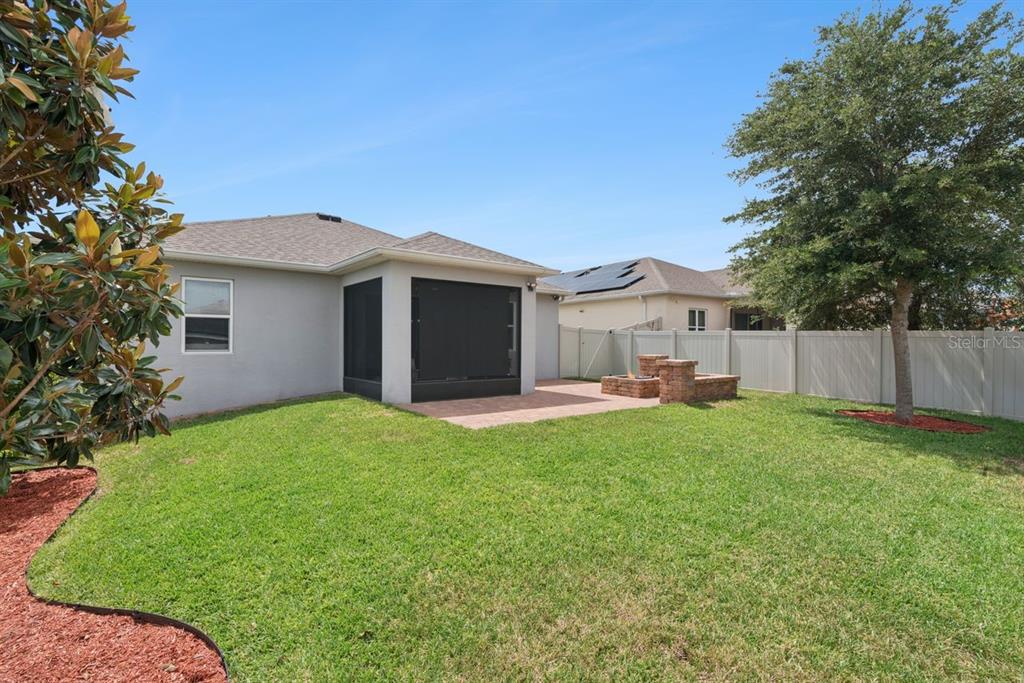 A backyard features a screened-in patio, a brick fire pit, and a white privacy fence — 206 HYDRA WAY, GROVELAND, FL