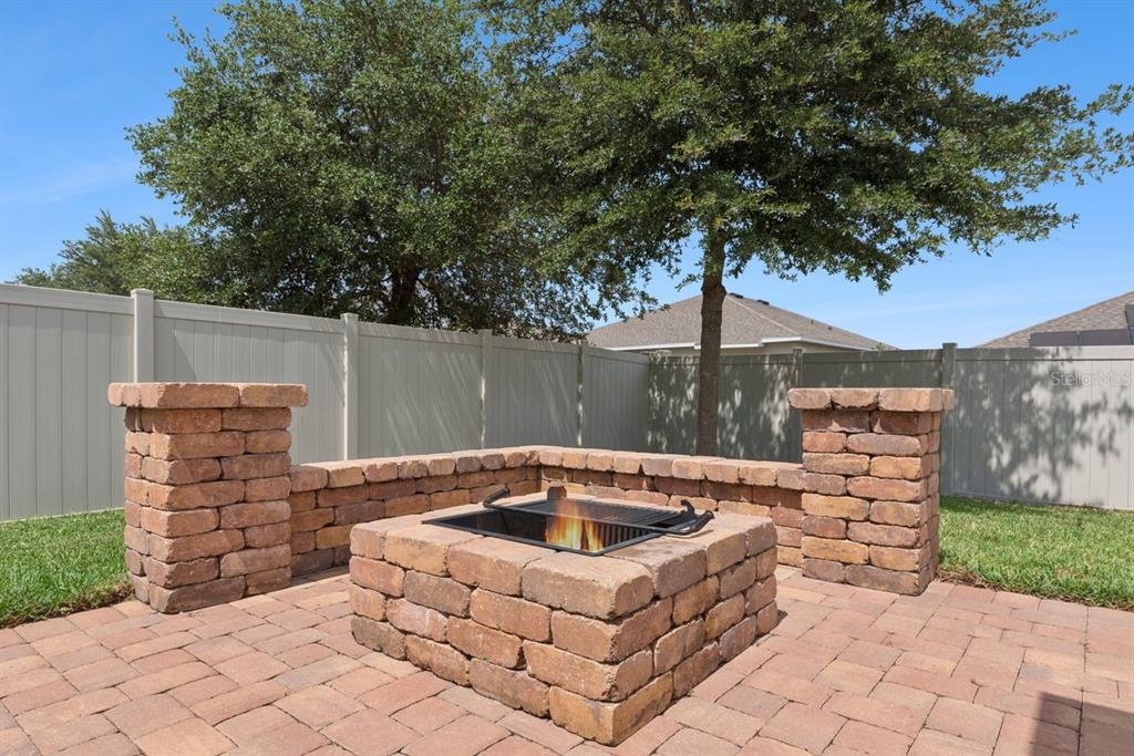 A stone fire pit with a metal grate sits on a paved patio in a backyard — 206 HYDRA WAY, GROVELAND, FL