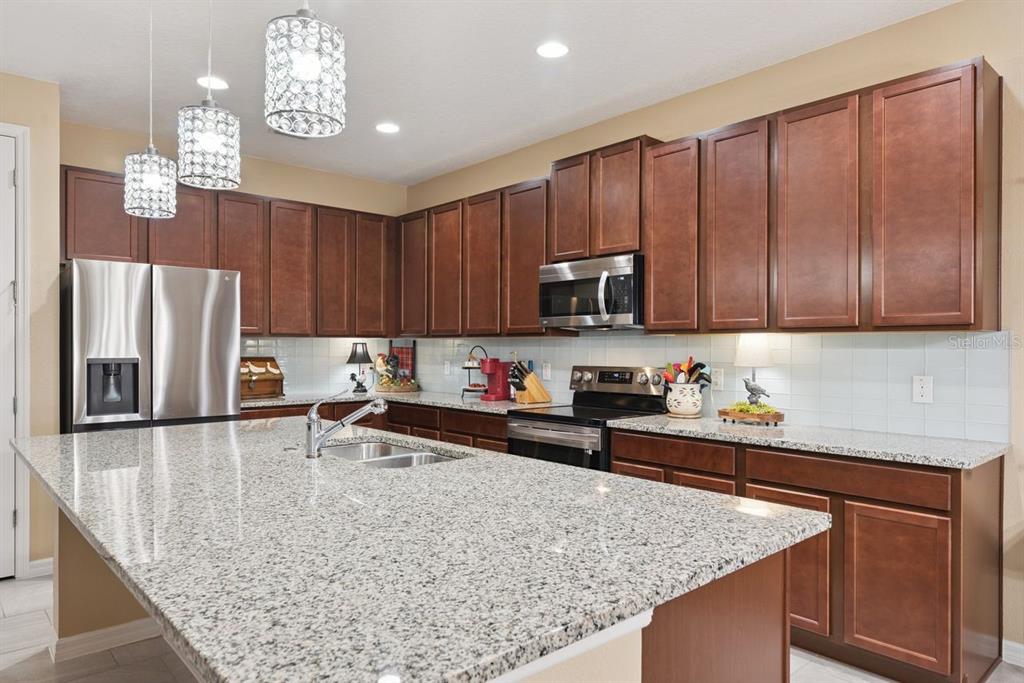 A kitchen with wood cabinets, granite countertops, stainless steel appliances, and three hanging pendant lights — 206 HYDRA WAY, GROVELAND, FL