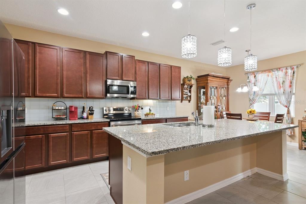 A kitchen features dark wood cabinets, granite countertops, a central island, and stainless steel appliances — 206 HYDRA WAY, GROVELAND, FL