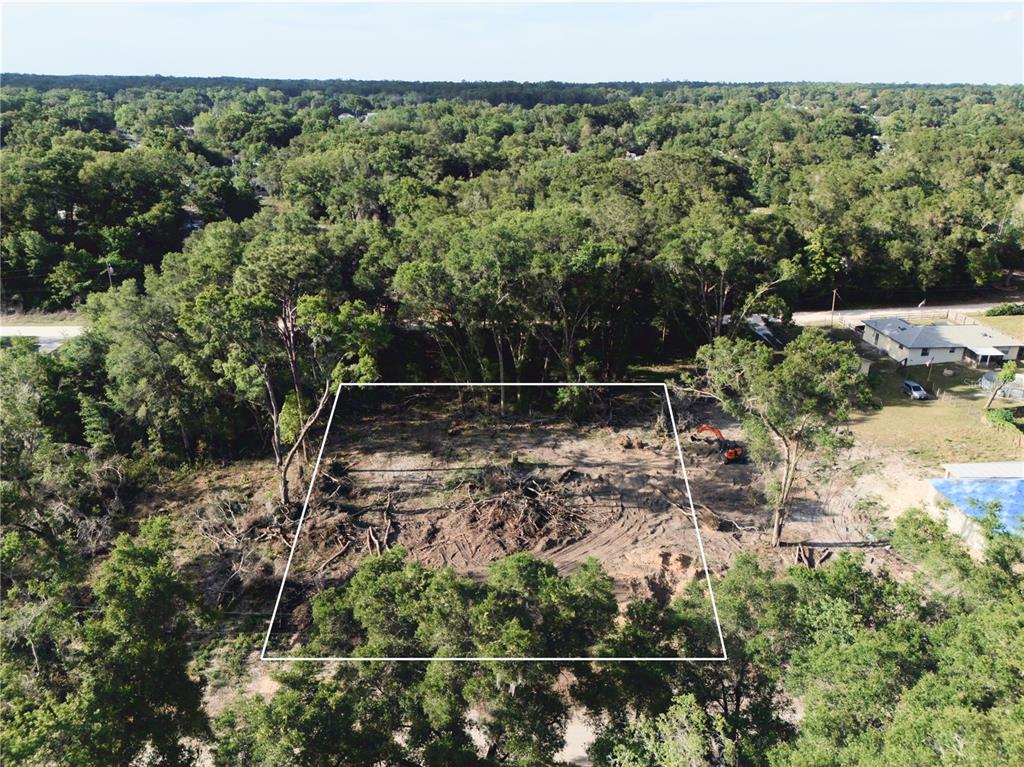 An aerial view shows a cleared, rectangular residential lot surrounded by trees and nearby houses — SE 140TH LANE, SUMMERFIELD, FL
