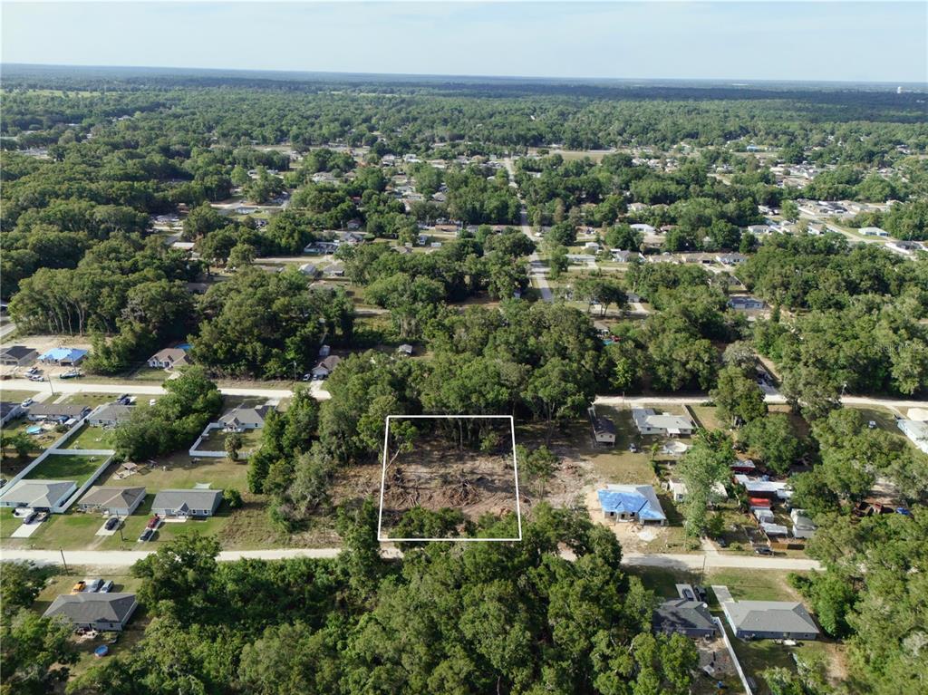 An aerial view shows a cleared, rectangular residential lot surrounded by trees and neighboring houses — SE 140TH LANE, SUMMERFIELD, FL