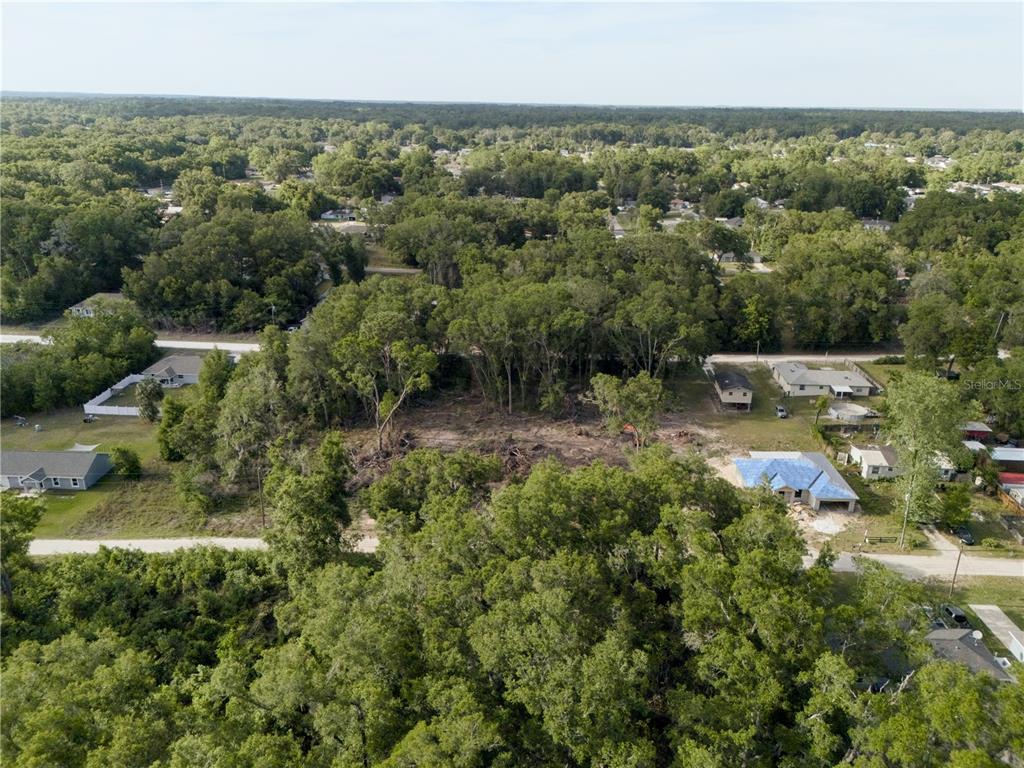 An aerial view shows a partially cleared wooded lot surrounded by residential houses and trees — SE 140TH LANE, SUMMERFIELD, FL