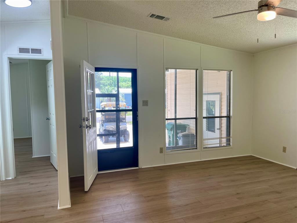 A living room with wood-look flooring, white walls, a ceiling fan, and a glass door — 603 ROBIN LANE, WILDWOOD, FL