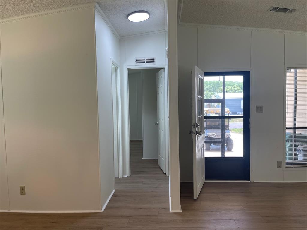 An interior view shows a hallway, a doorway leading outside, and light-colored wood-look flooring — 603 ROBIN LANE, WILDWOOD, FL