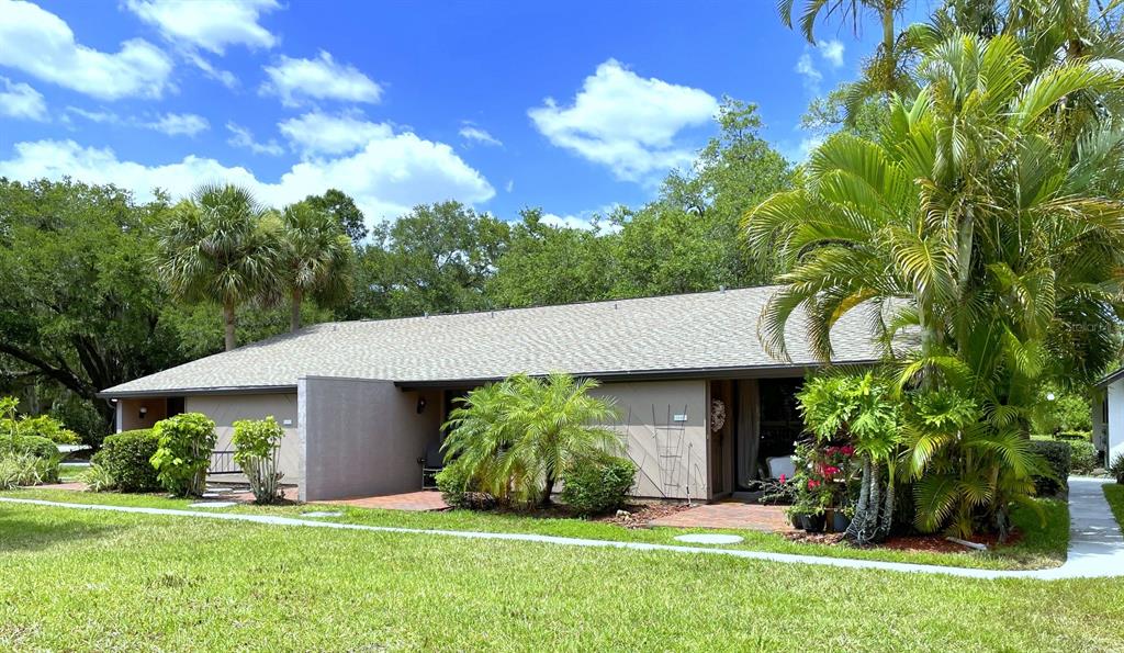 A single-story residential building with a gray roof, tan exterior, and lush tropical landscaping — 3543 LONGMEADOW UNIT 22, SARASOTA, FL