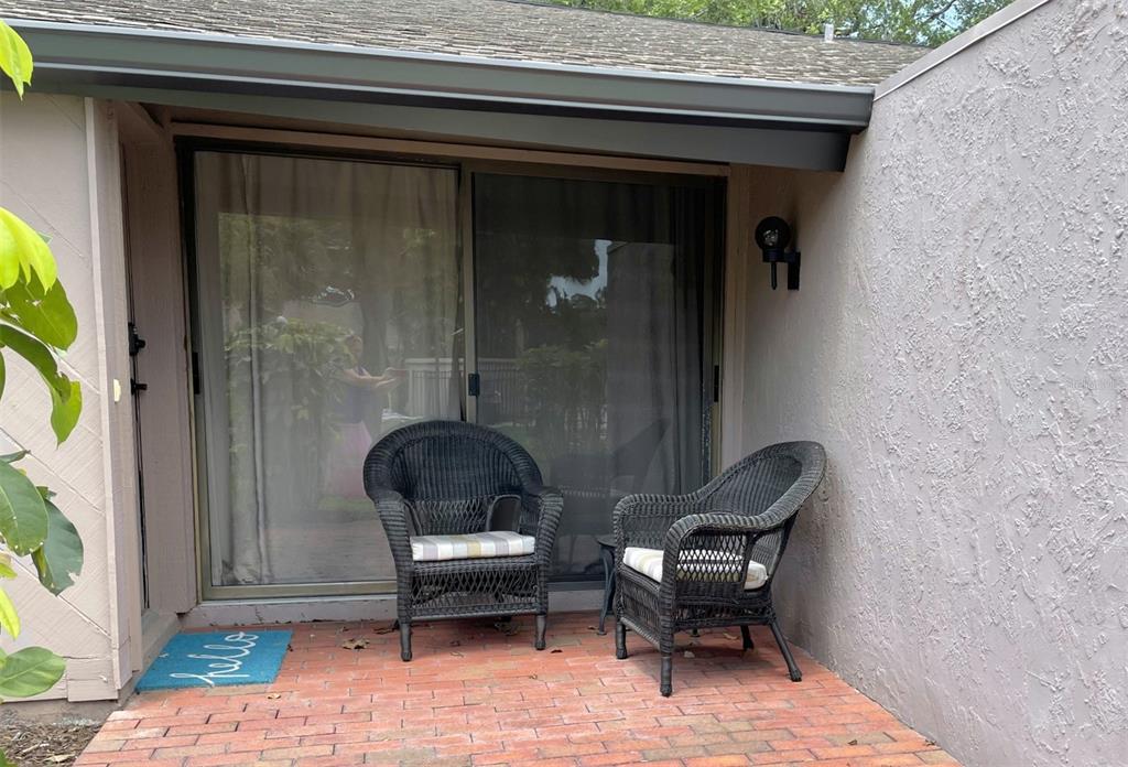 A brick patio features two wicker chairs in front of a sliding glass door — 3543 LONGMEADOW UNIT 22, SARASOTA, FL