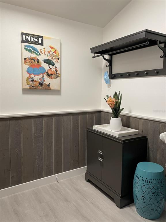 An entryway features gray wood paneling, a dark cabinet, a wall-mounted rack, and beach-themed art — 3543 LONGMEADOW UNIT 22, SARASOTA, FL