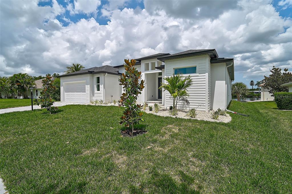 A modern white single-story house with a two-car garage and landscaped front yard — 6655 PAN AMERICAN BOULEVARD, NORTH PORT, FL