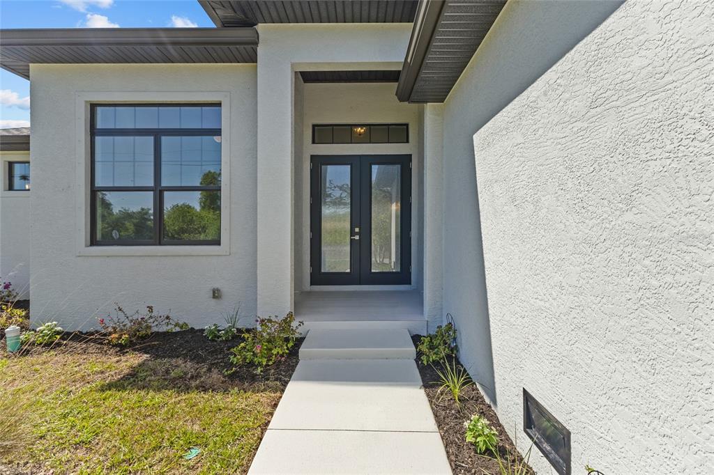 A modern house exterior features a white stucco facade, dark trim, and a double-door entrance — 12396 BACCHUS ROAD, PORT CHARLOTTE, FL