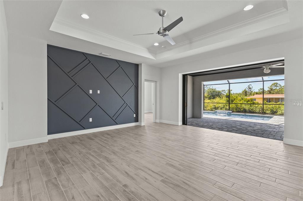 A living room features a dark geometric accent wall, light wood-look tile, and a pool view — 12396 BACCHUS ROAD, PORT CHARLOTTE, FL