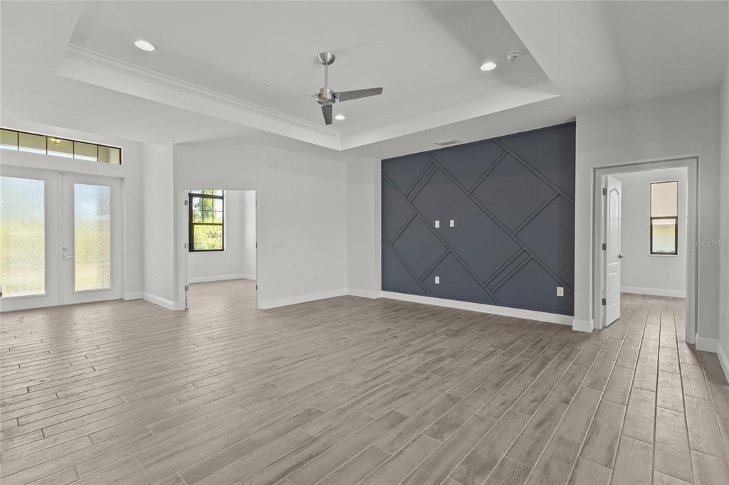A living room features light wood-look tile flooring, a tray ceiling, and a blue accent wall — 12396 BACCHUS ROAD, PORT CHARLOTTE, FL