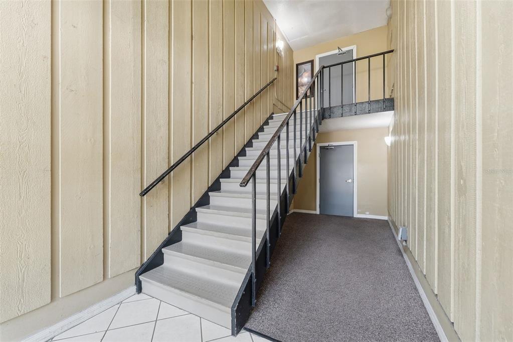 An indoor staircase with metal railings leads to an upper landing between two gray doors — 1695 LEE ROAD UNIT B204, WINTER PARK, FL