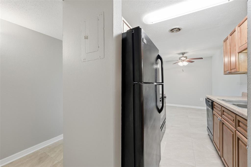 A kitchen with wood cabinets, black appliances, and light tile flooring opens to a dining area — 1695 LEE ROAD UNIT B204, WINTER PARK, FL
