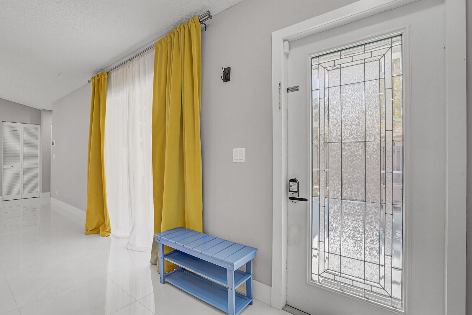 A bright entryway features a blue shoe bench, yellow curtains, and a glass-paneled front door — 1329 Periwinkle Place, Wellington FL 33414, WELLINGTON, FL
