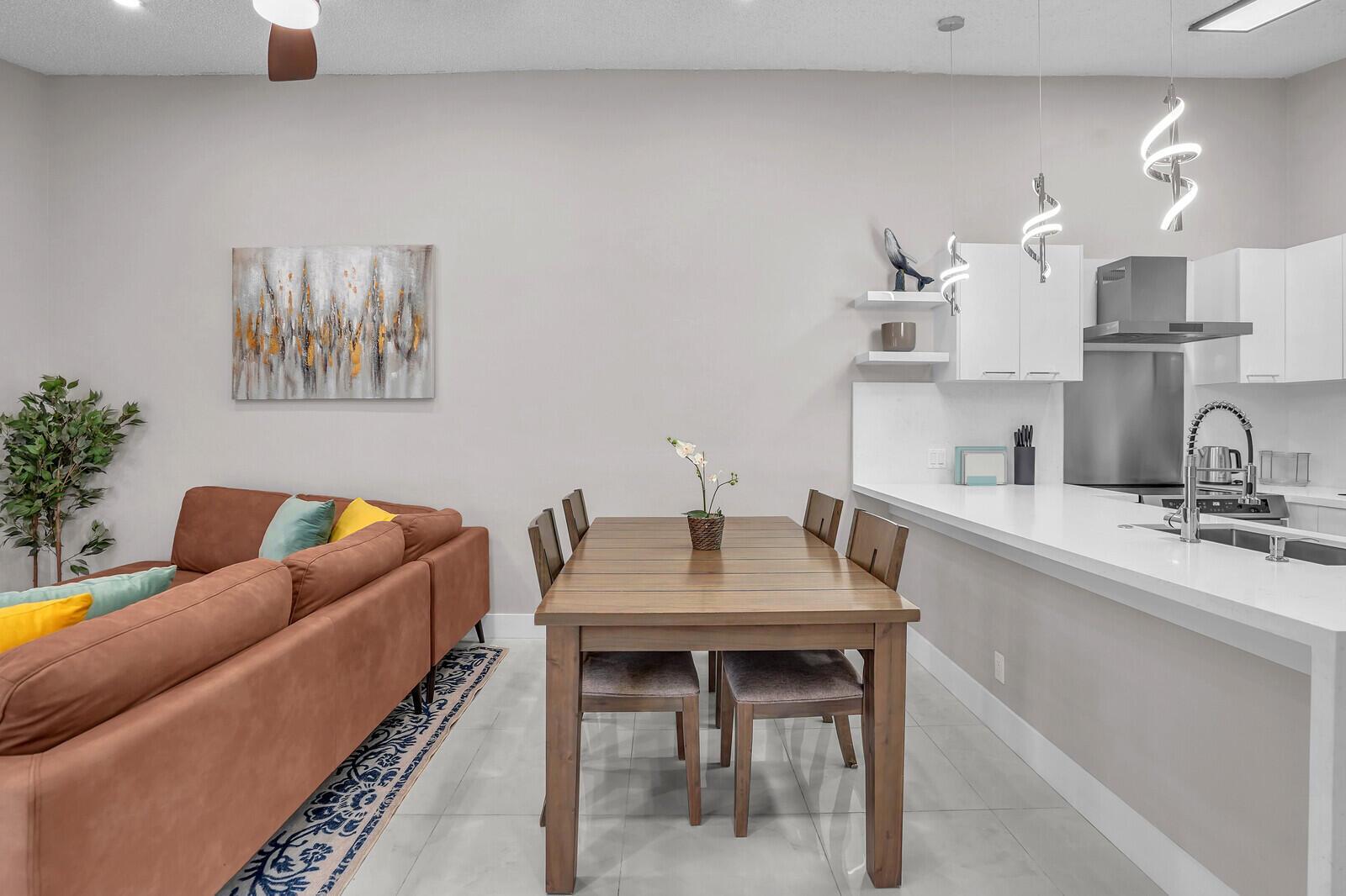 A dining area with a wooden table sits between a brown sofa and a white kitchen — 1329 Periwinkle Place, Wellington FL 33414, WELLINGTON, FL
