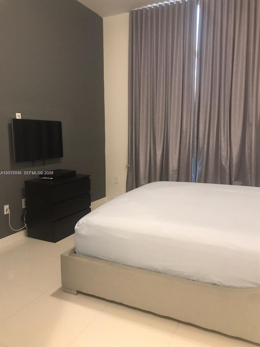 A bedroom features a bed, a black dresser, a wall-mounted television, and floor-to-ceiling curtains — 7751 NW 107th Ave # 803, Doral FL 33178, DORAL, FL