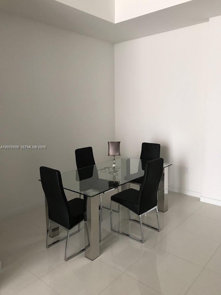 A glass-topped dining table with four black chairs sits in a minimalist room — 7751 NW 107th Ave # 803, Doral FL 33178, DORAL, FL