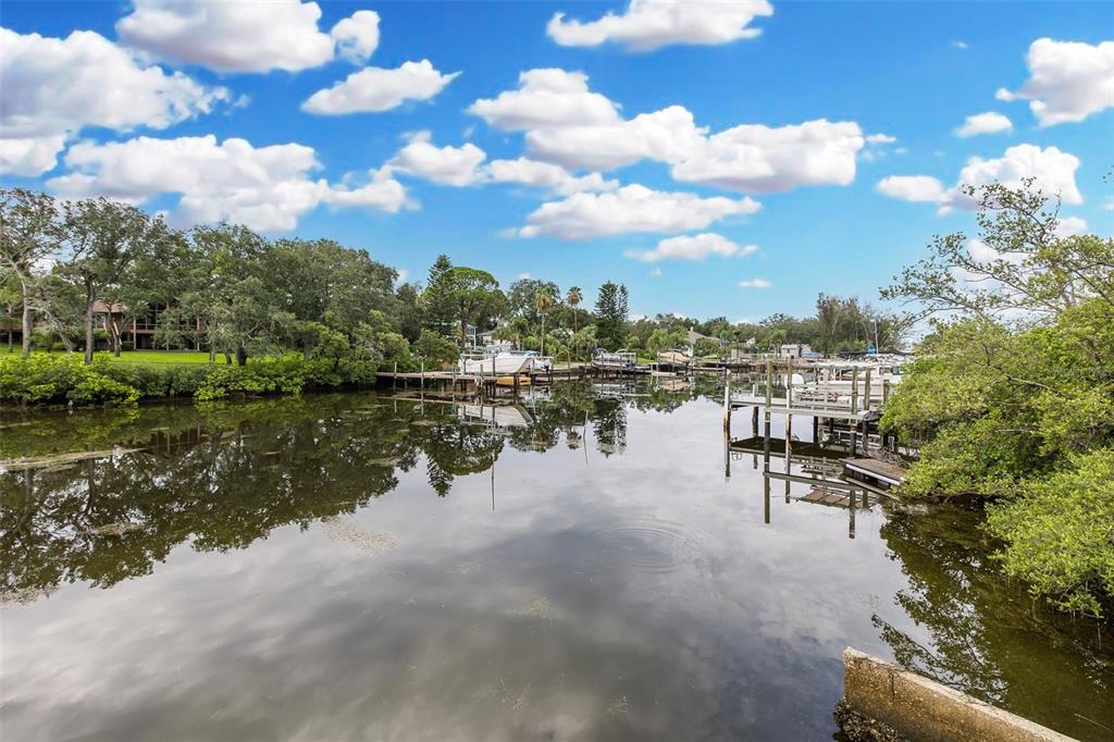 A calm canal reflects the sky, surrounded by lush trees, boat docks, and moored vessels — 2030 GULFVIEW DRIVE, HOLIDAY, FL