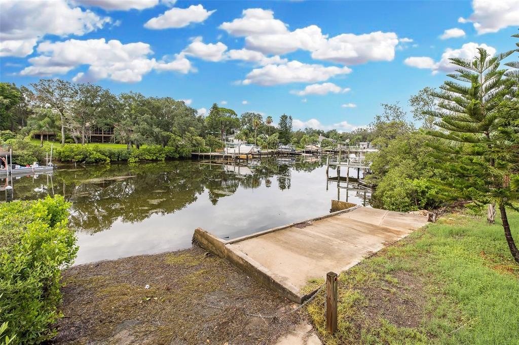A concrete boat ramp leads into a calm canal surrounded by trees and wooden docks — 2030 GULFVIEW DRIVE, HOLIDAY, FL