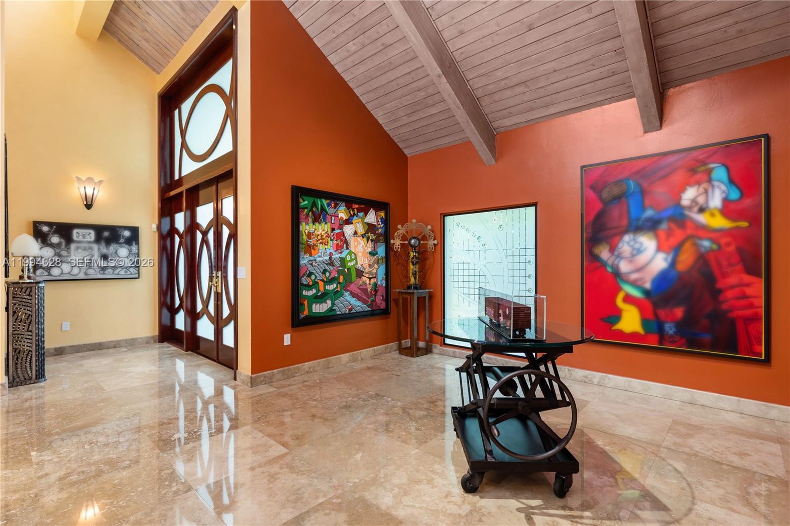 A foyer features vaulted wood-beam ceilings, orange walls, marble floors, and large contemporary art pieces — 20251 W Oak Haven Cir, Miami FL 33179, MIAMI, FL