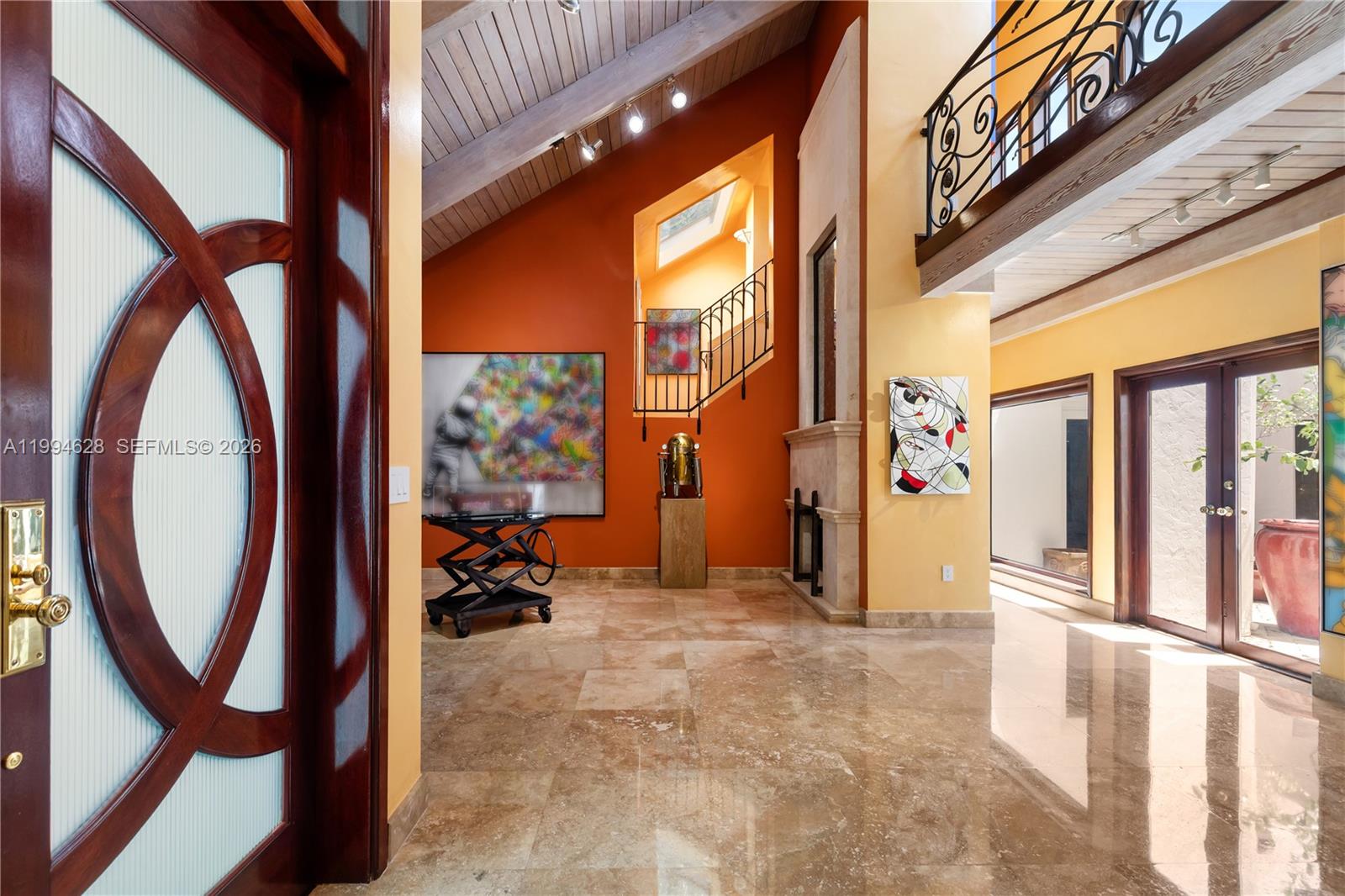 A high-ceilinged foyer features orange walls, marble floors, a staircase, and modern art pieces — 20251 W Oak Haven Cir, Miami FL 33179, MIAMI, FL