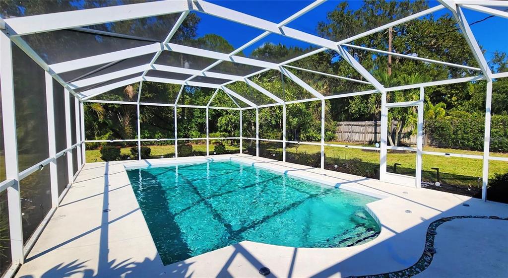 A rectangular swimming pool is enclosed by a white metal screen cage in a backyard — 329 BERNARD AVENUE, SARASOTA, FL