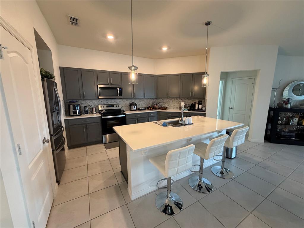 A kitchen features dark gray cabinetry, a white quartz island with three stools, and tile flooring — 1127 SEEDORF DRIVE, WINTER HAVEN, FL