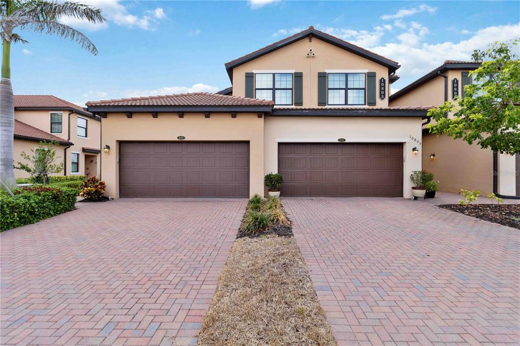 A two-story residential building with two brown garage doors and a brick paver driveway — 10805 TARFLOWER DRIVE UNIT 101, VENICE, FL